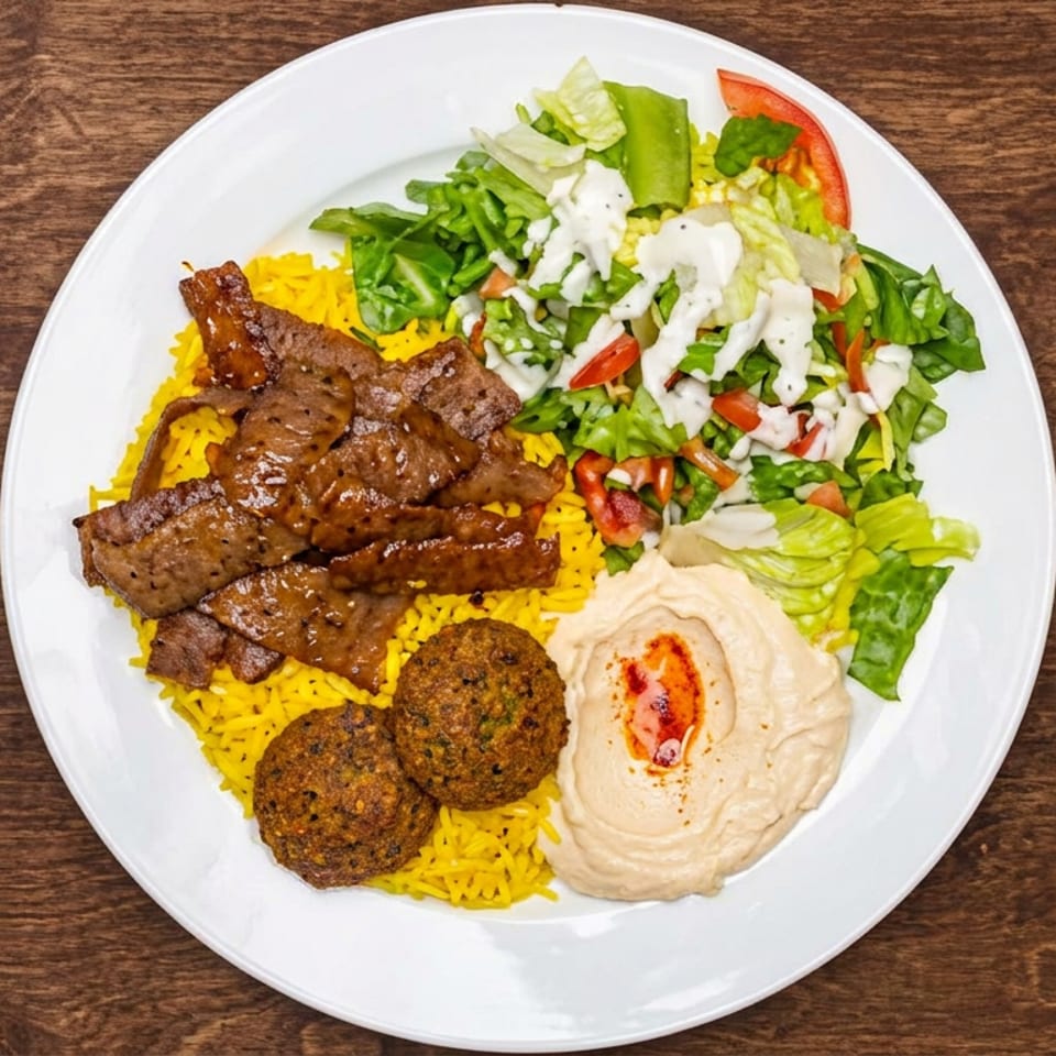 Middle Eastern platter with yellow rice, grilled beef, falafel, hummus, and dressed salad on a white plate.
