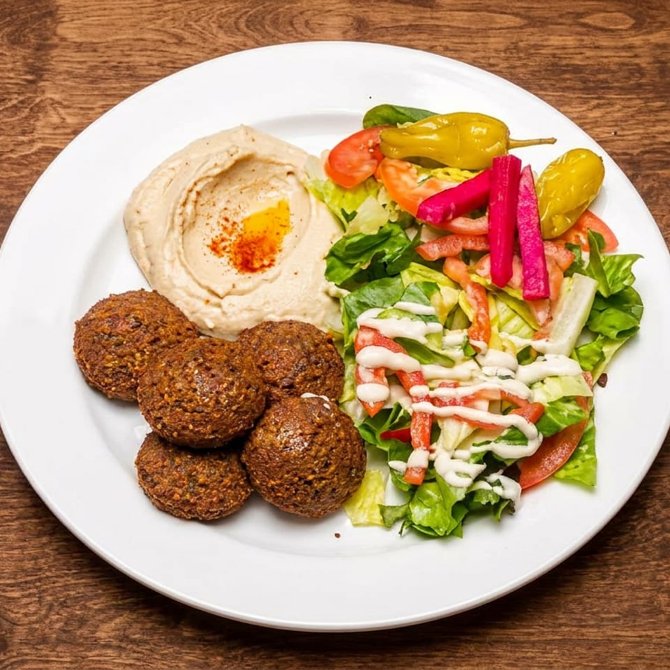 Plate of falafel, hummus, salad with creamy dressing, tomatoes, lettuce, and pickled vegetables on a wooden table.